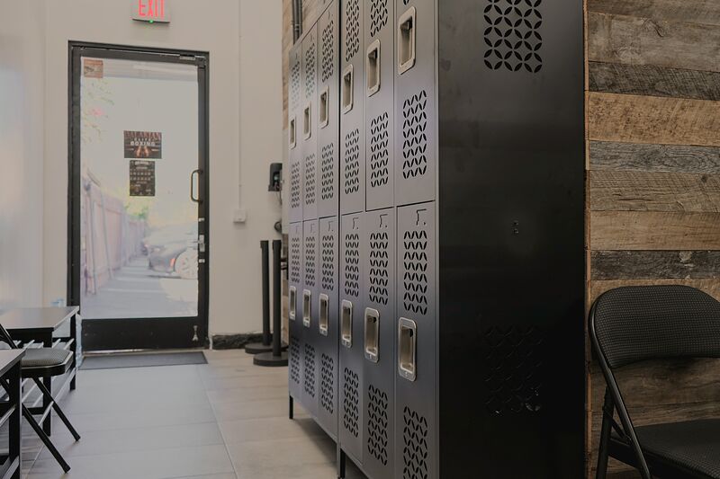 A row of black perforated metal lockers beside the glass back door, with folding chairs and a table opposite