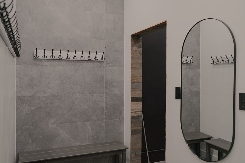 Changing room with grey stone-look tile, a slatted bench, rows of coat hooks and a tall oval mirror