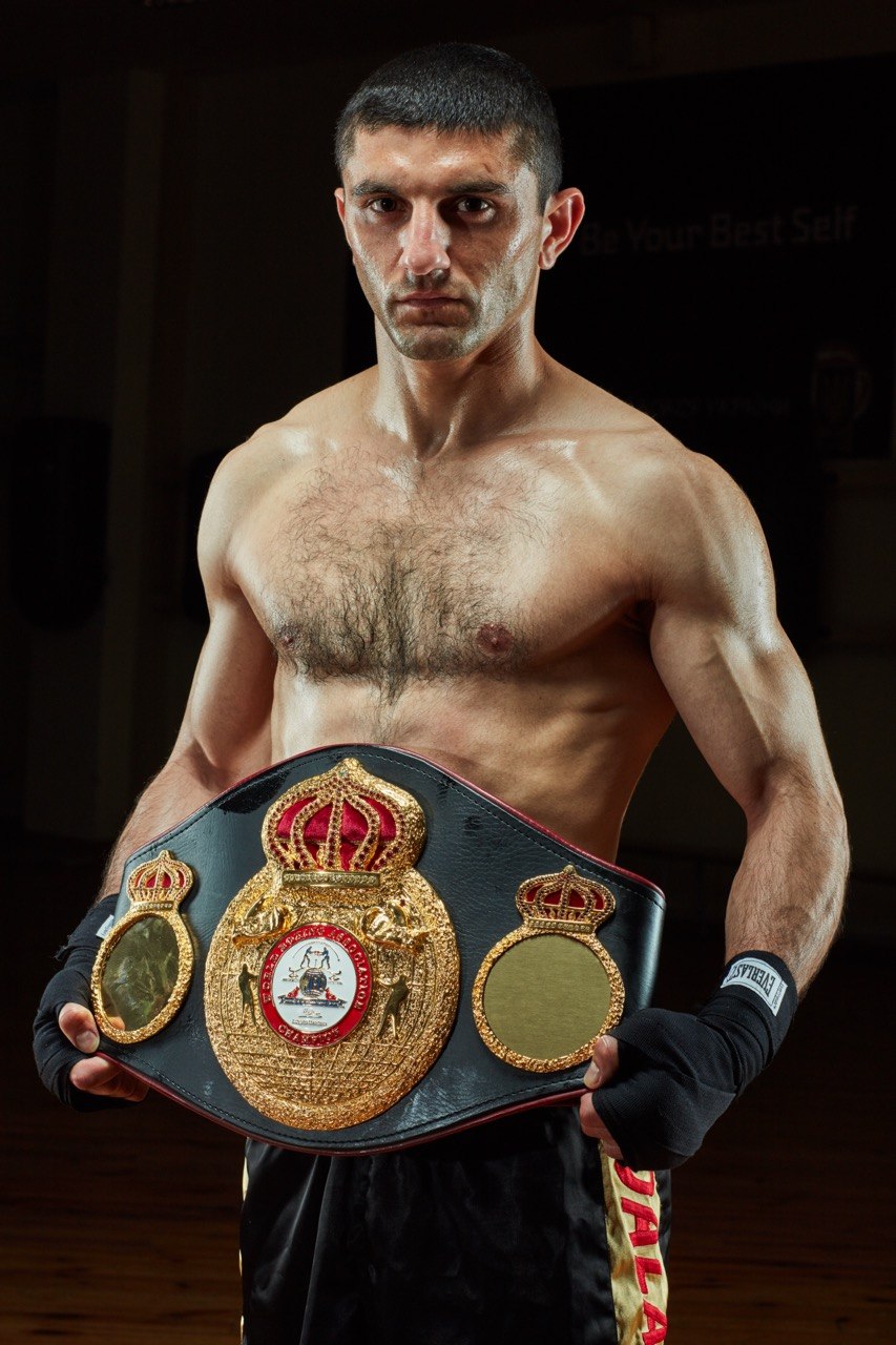 Artem Dalakian holding the WBA world championship belt at chest height, looking straight at the camera